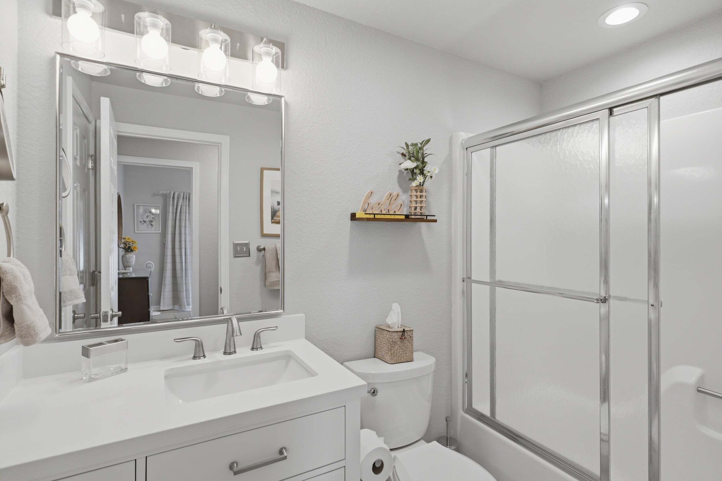 A bathroom with a white sink, mirror, and toilet. There is a shower with a glass door.