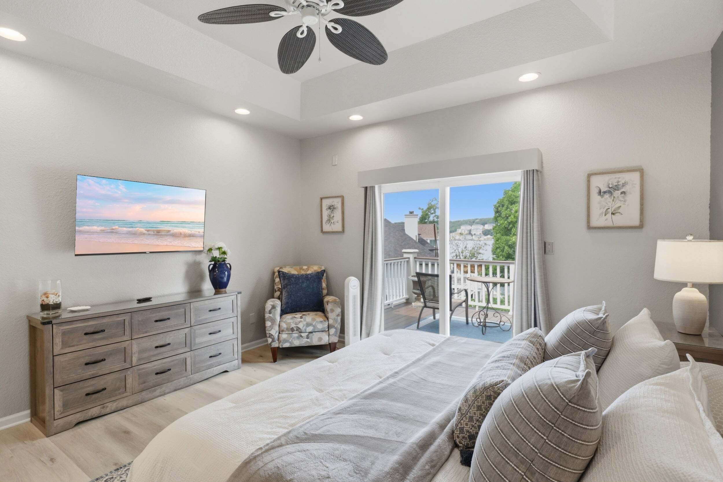 A bedroom with a large bed, a dresser, a chair, a TV, and a balcony with a view.