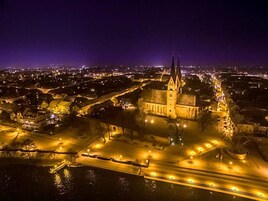 Vista aérea de un paisaje urbano nocturno con una iglesia destacada que presenta dos torres, rodeada de calles e edificios iluminados.