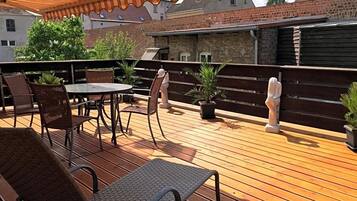 Eine Terrasse im Freien mit Tisch und Stühlen, ein Holzboden und eine Backsteinmauer im Hintergrund.