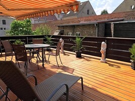 Un patio al aire libre con una mesa y sillas, una terraza de madera y un muro de ladrillo al fondo.