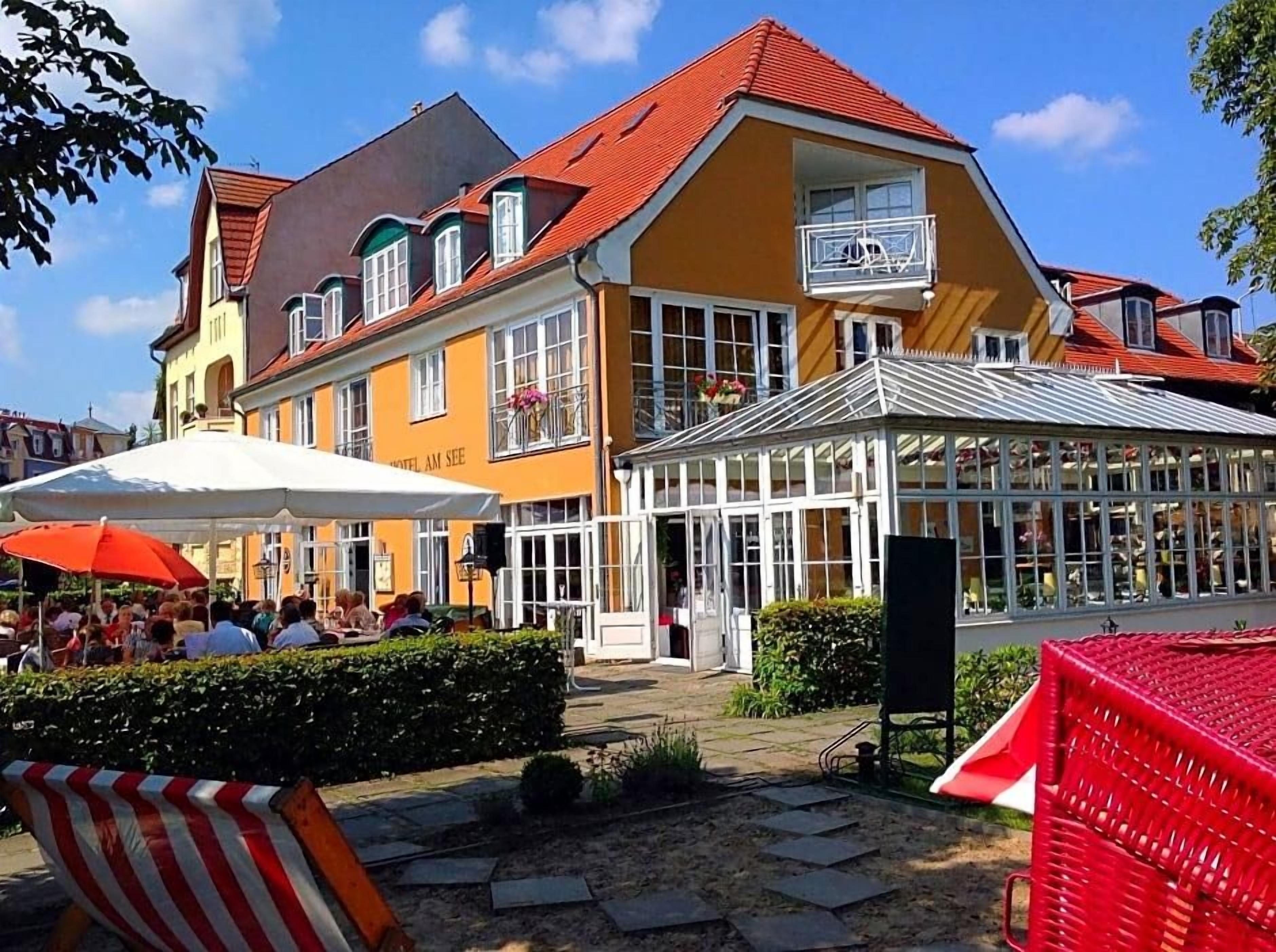 A hotel with a yellow facade, a red roof, and a covered outdoor seating area with umbrellas.