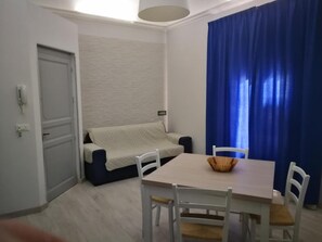 A compact room with a sofa, a dining table, and chairs. - Emporium Case Vacanze (Castellammare del Golfo)