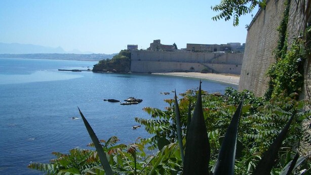 A coastal view with a fortified structure, a beach, and dense vegetation. - Emporium Case Vacanze (Castellammare del Golfo)
