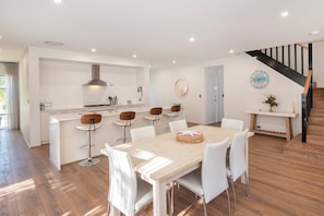A modern kitchen with white cabinetry, a central island, and bar stools. - The Milly (Dunsborough)