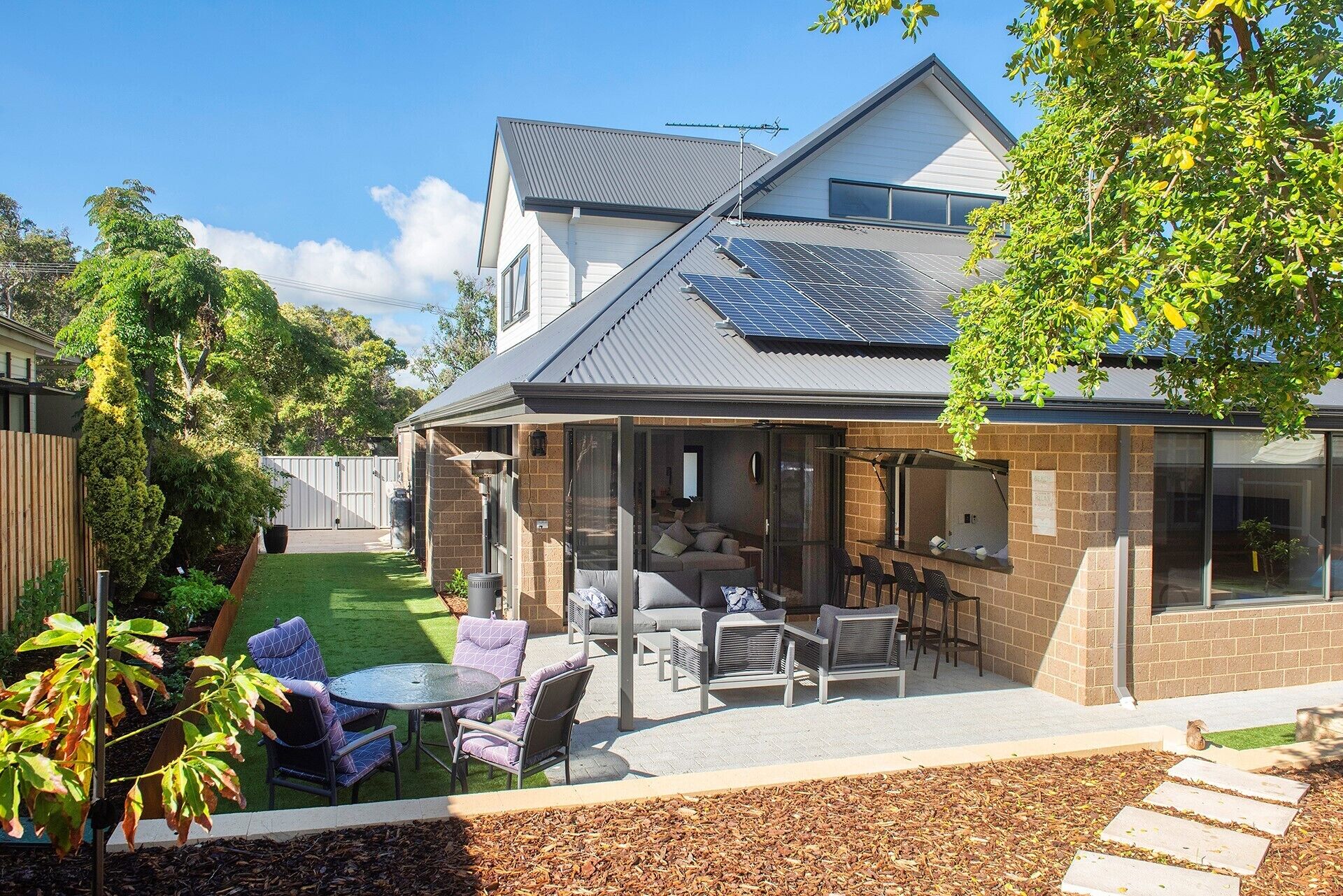 Een woonhuis met een overdekte patio, een zitgedeelte buiten en zonnepanelen op het dak.