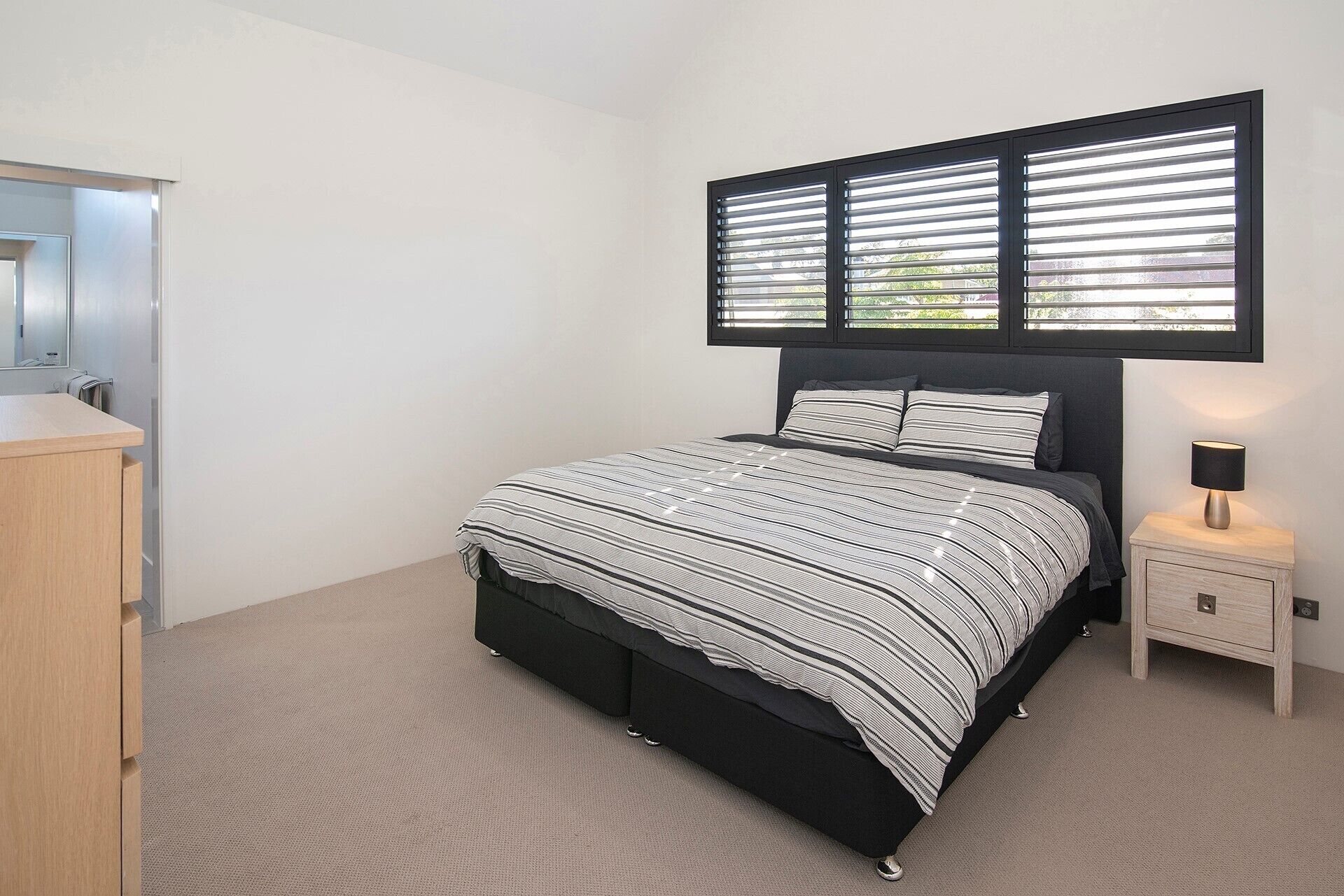 A bedroom with a bed, a nightstand, a lamp, and a window with blinds.
