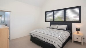Quarto com cama, mesa de cabeceira, luminária e janela com persianas.