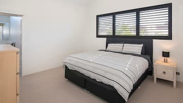 A bedroom with a bed, a nightstand, a lamp, and a window with blinds.