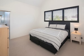 A bedroom with a bed, a nightstand, a lamp, and a window with blinds. - The Milly (Dunsborough)