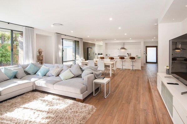 A modern living room with a sectional sofa, a dining area with bar stools, and a kitchen with a central island. - The Milly (Dunsborough)