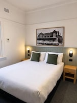 Una habitación de hotel con una cama grande, dos mesitas de noche, una lámpara de pared y un cuadro enmarcado sobre la cama.