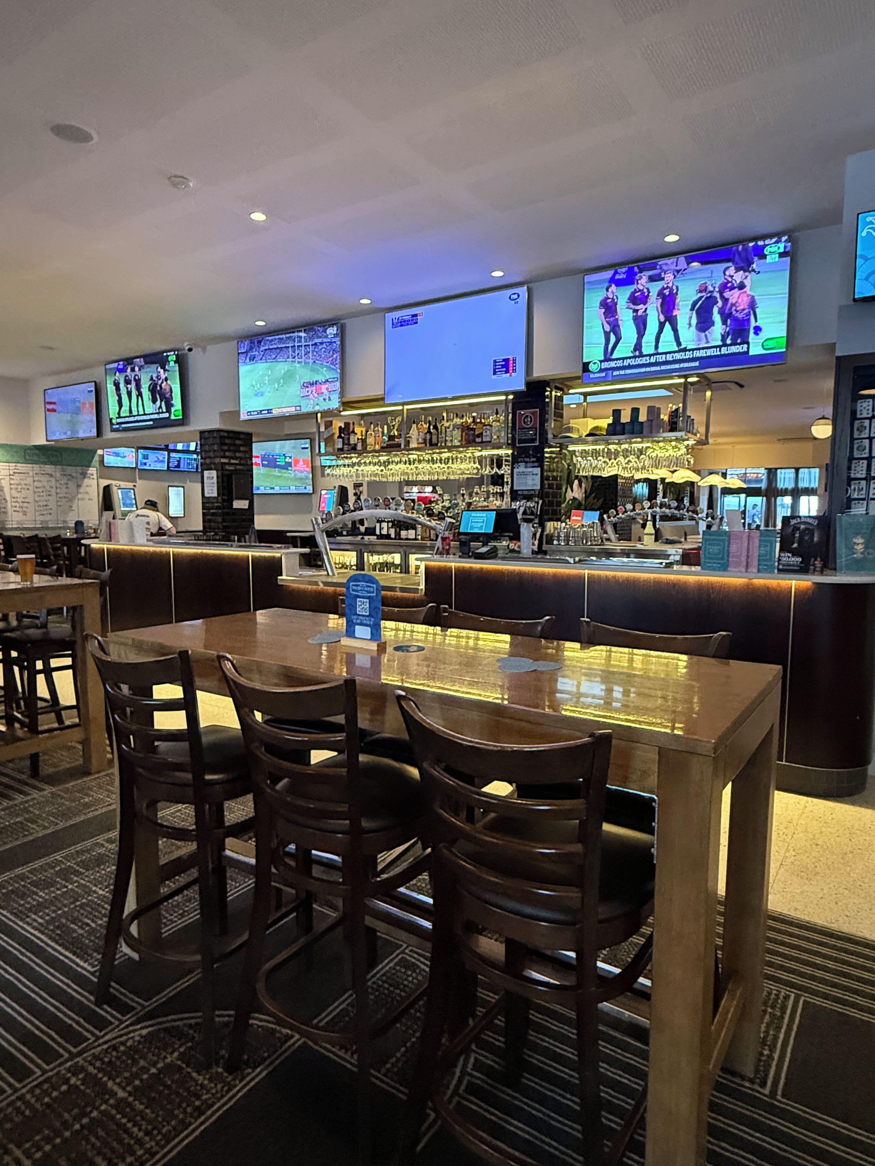 A bar area with multiple screens displaying sports events, a bar counter, and seating arrangements.