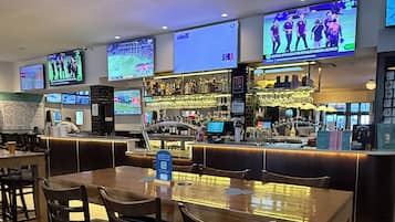 A bar area with multiple screens displaying sports events, a bar counter, and seating arrangements.