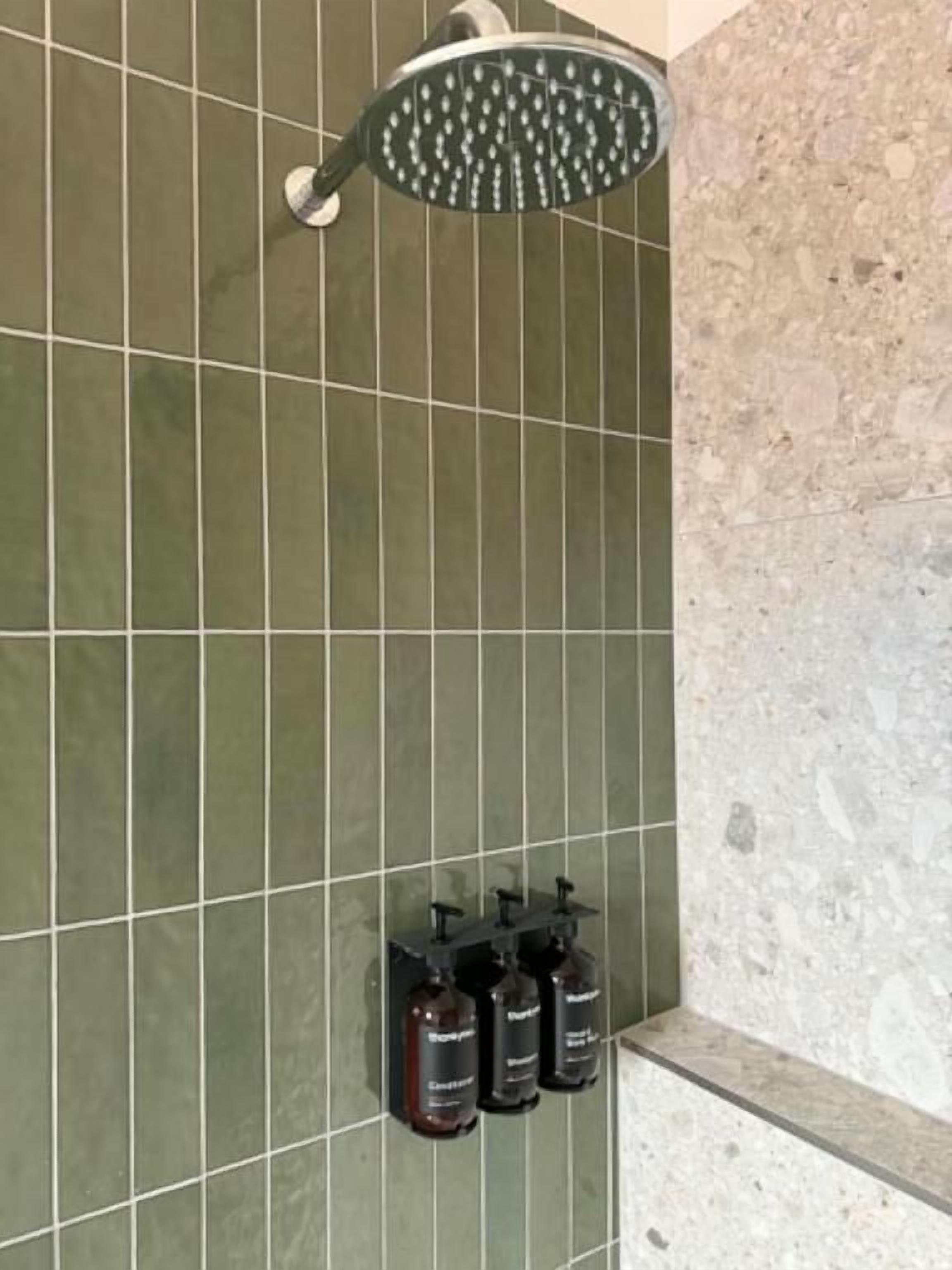 Zona de ducha con cabezal de ducha de mano y tres botellas de champú en un estante adosado a la pared.