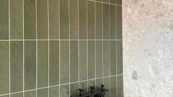 Zona de ducha con cabezal de ducha de mano y tres botellas de champú en un estante adosado a la pared.