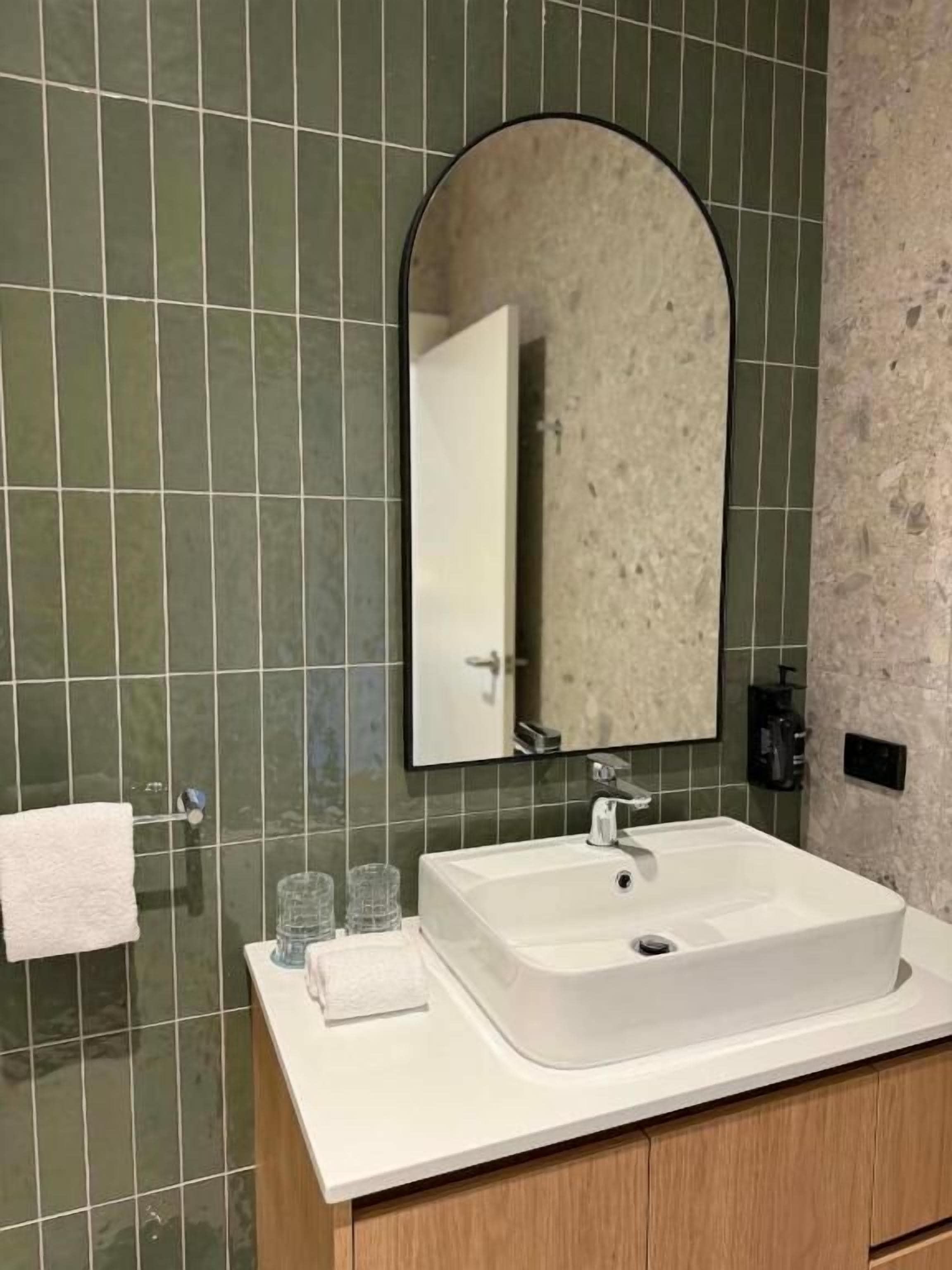 A bathroom with a white sink, a mirror, and green tiled walls.