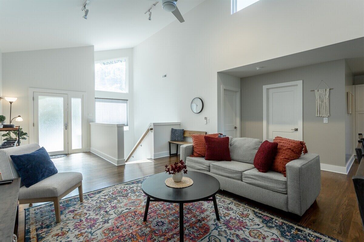 A spacious living room with a grey sofa, a round coffee table with a vase, and a patterned rug.