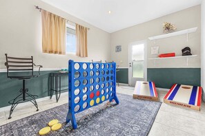 Ein Zimmer mit einem blauen und gelben Spieltisch, einem stahlrohrgestellten Stuhl, einem kleinen Tisch mit Stuhl und einer Tür mit Fenster.