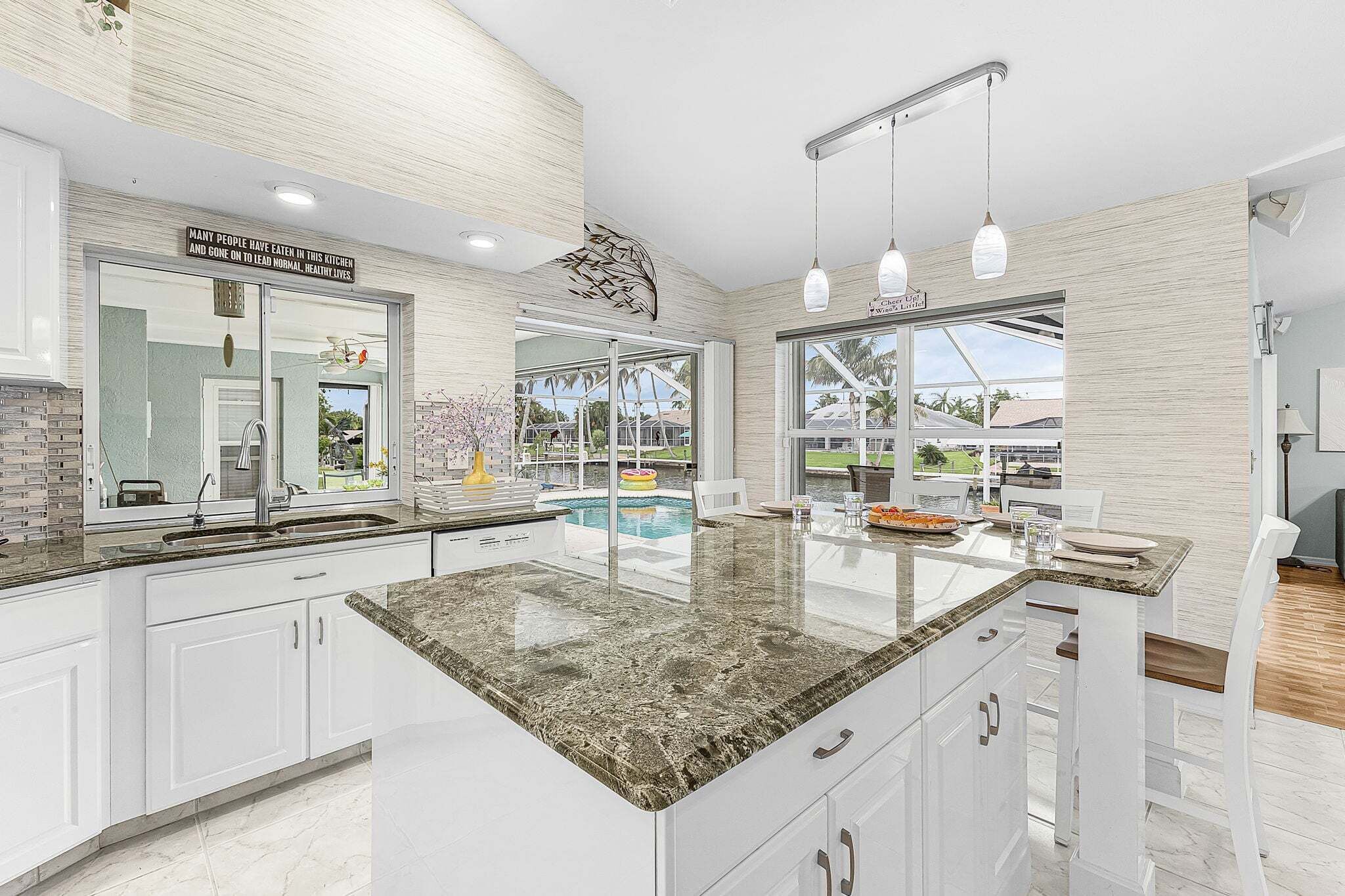A modern kitchen with a large island, a view of a pool, and a sign above the sink.