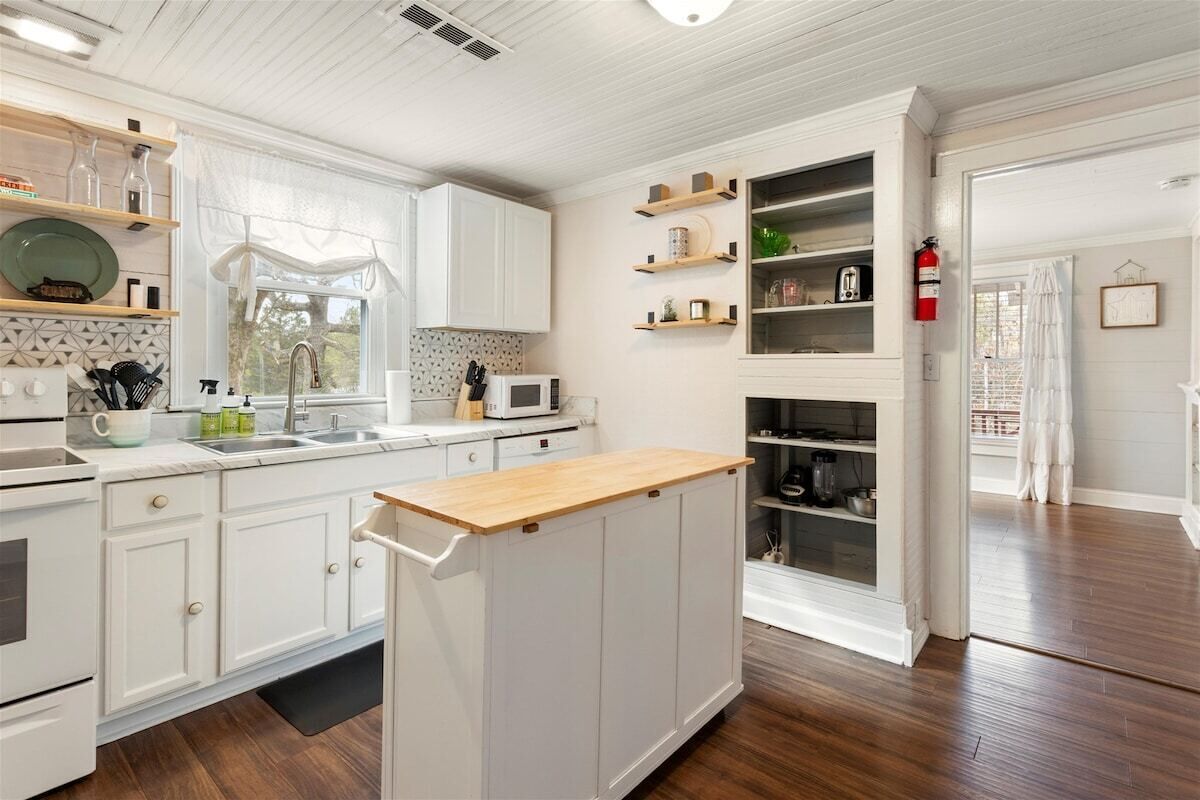 A modern kitchen with white cabinetry, a wooden island, and built-in shelves.