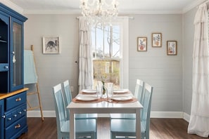 A dining room with a white table set for four, blue chairs, a chandelier, and a blue cabinet. - Lucky's Cottage | Hot Tub+Dog Friendly+Fire Pit (Rossville)