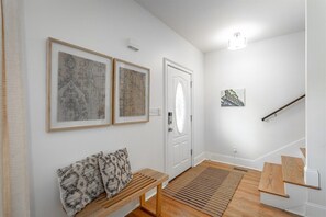 Ein Flur mit einer hölzernen Sitzbank, einem gemusterten Teppich und zwei gerahmten Kunstwerken an der Wand.