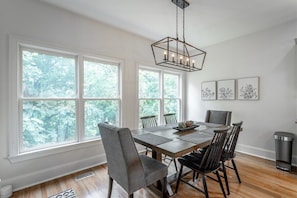 A dining room with a large table, chairs, and a chandelier. There are windows with a view of trees. - Oliver's Landing | Walk Right to North Shore! (Chattanooga)