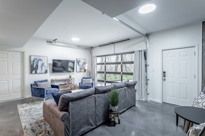 Ein modernes Wohnzimmer mit einem Ecksofa, einem Flachbildfernseher und einem großen Fenster mit Vorhängen.