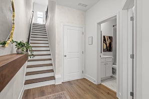 A staircase with wooden steps and a white door, leading to a bathroom with a toilet and sink. - Near Downtown & Lookout Mtn | Game Room | Designer (Chattanooga)