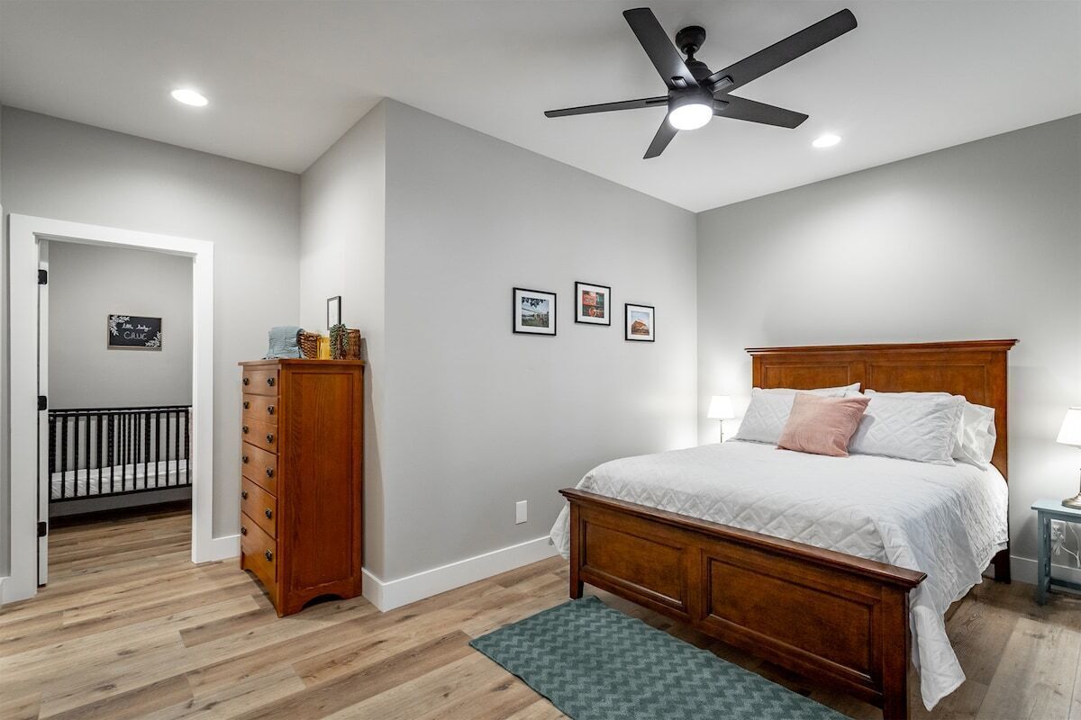 Une chambre à coucher avec un lit en bois, un ventilateur de plafond, une commode et un berceau dans la pièce adjacente.