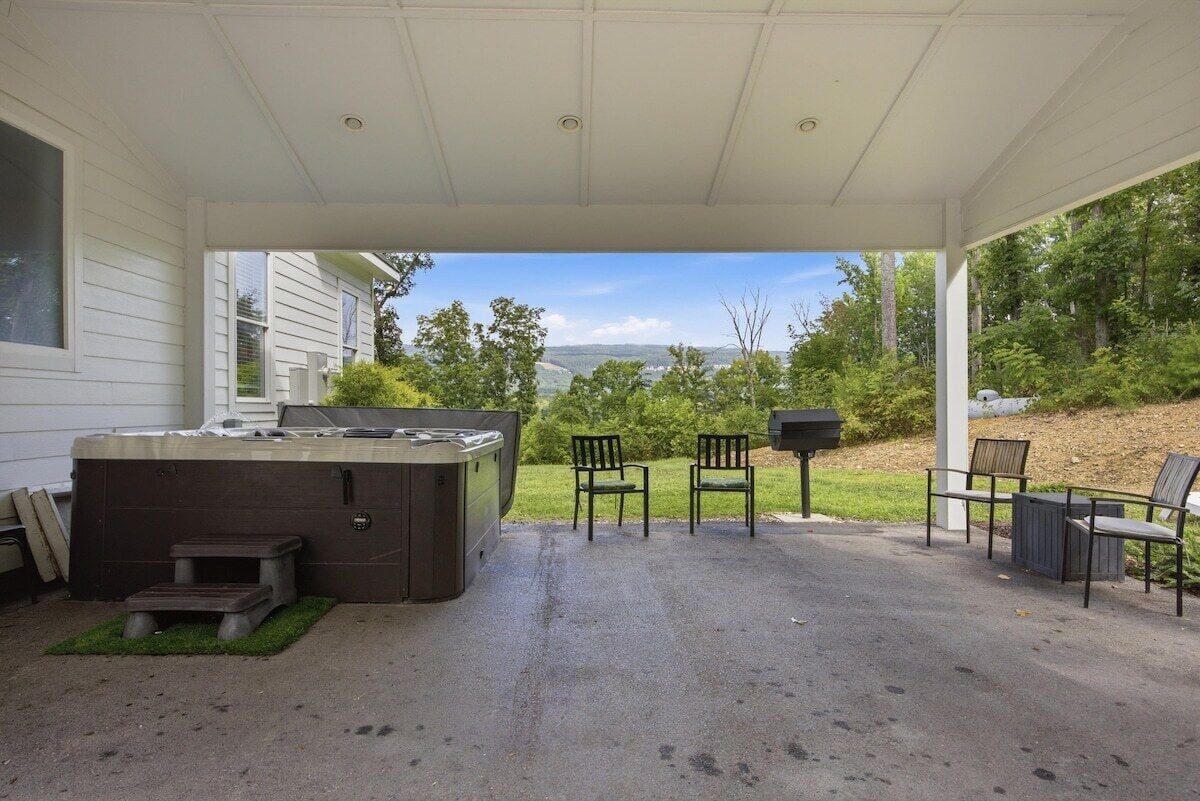 A covered patio area with a hot tub, outdoor seating, and a view of a wooded landscape.