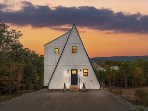 A white, triangular-roofed building with a number '928' on the front door, surrounded by trees and a clear sky. - Urban Vista | A-Frame | Theatre + Pet Baby Goats! (Rossville)