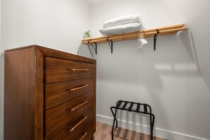 A bedroom with a wooden dresser, a metal rack with a pillow, and a black chair. - Urban Vista | A-Frame | Theatre + Pet Baby Goats! (Rossville)