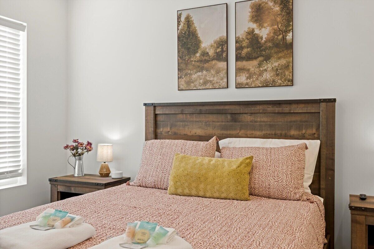 Una camera da letto con una testiera in legno, un letto con biancheria a motivi, un comodino con una lampada e due quadri appesi al muro.