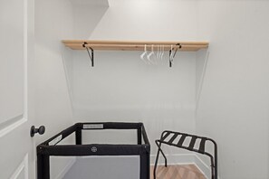 Ein Zimmer mit einem schwarzen Metall-Kinderbett, einem Holzregal mit Kleidung und einer Tür.