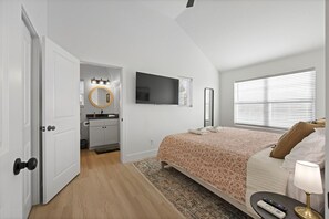 Ein Schlafzimmer mit einem Bett, einem Fernseher, einem Spiegel und einer Tür zu einem Badezimmer.