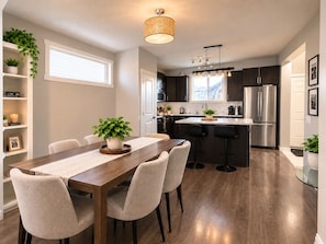 A modern kitchen with a dining area, featuring a wooden table, chairs, and a hanging light fixture. - Family-Friendly 5BR Home| Basement Included (Edmonton)