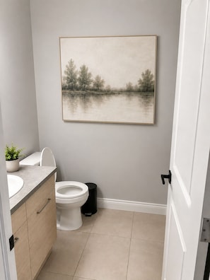 A bathroom with a toilet, sink, and cabinet, a painting on the wall, and a potted plant. - Family-Friendly 5BR Home| Basement Included (Edmonton)
