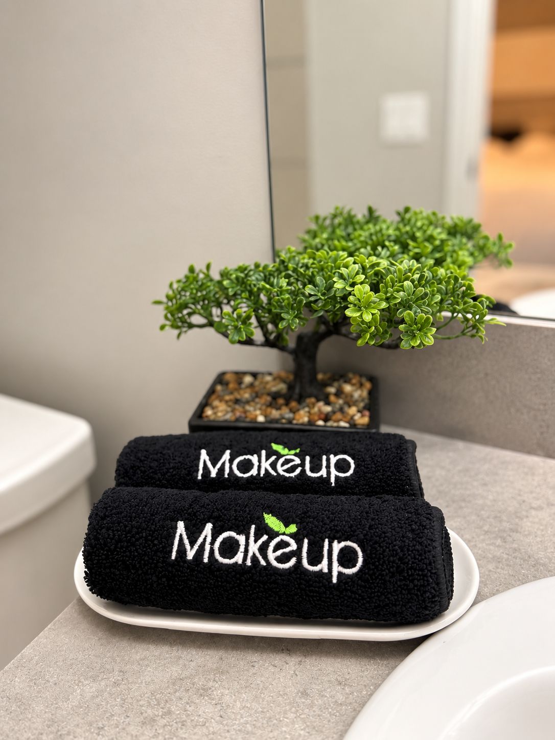 Ein Badezimmer mit einem kleinen Topfpflanzen, zwei Handtüchern mit der Aufschrift 'Makeup' und einem weißen Waschbecken.