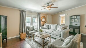 Ein Wohnzimmer mit einer Couch, Sesseln, einem Couchtisch, einem Deckenventilator und einem Fenster mit Vorhängen.