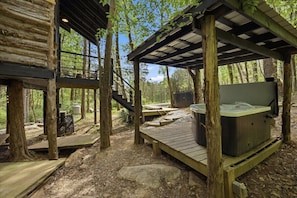 A wooden deck with a hot tub, surrounded by trees and a covered area with a staircase. - Cedarbrook Treehouse | Rustic Escape • Hot Tub! (Trenton)