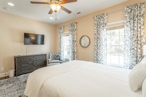 Quarto com cama, cômoda, televisão, ventilador de teto e cortinas florais.