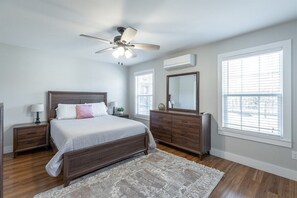 A bedroom with a wooden bed, a ceiling fan, a dresser, and a large window with blinds. - 2 Apartments with Country Views | Dog Friendly! (Rossville)