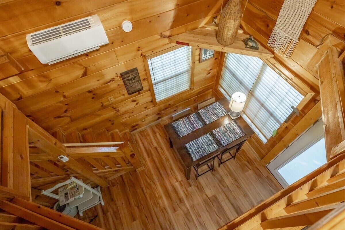 A wooden cabin interior with a ceiling fan, air conditioning unit, and a dining table with a patterned tablecloth.