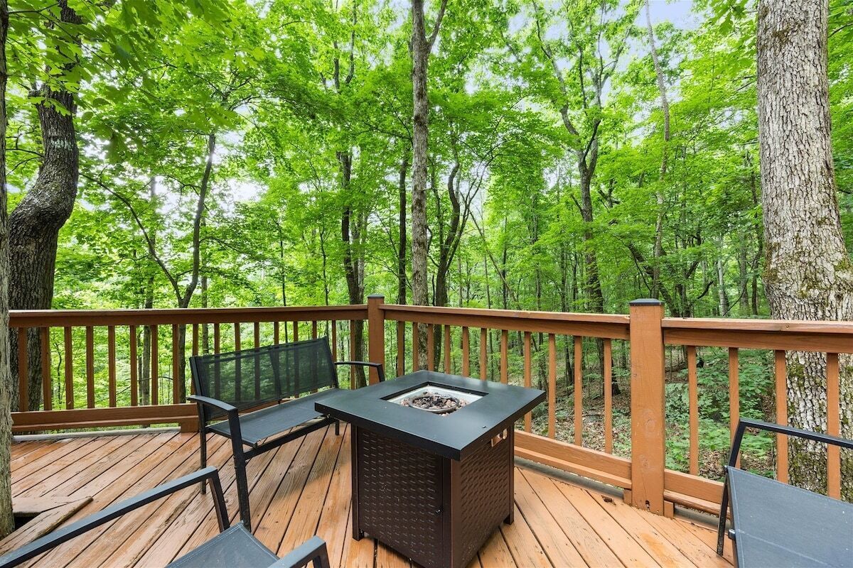 A deck with a fire pit, seating, and a view of a forest.