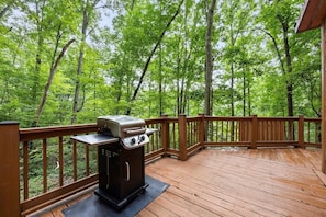 Eine Holzterrasse mit Grill und Blick auf einen Wald.