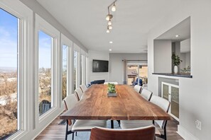A spacious dining area with a large wooden table, white chairs, and a view through large windows. - Crestview Heights | Stunning City Views | Hot Tub (Chattanooga)
