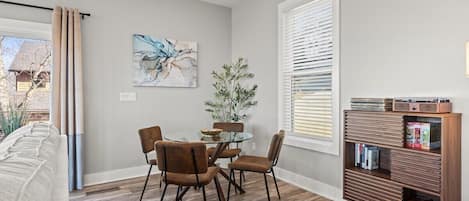 Uma área de refeições com mesa de vidro, cadeiras marrons, estante de livros e um quadro na parede.