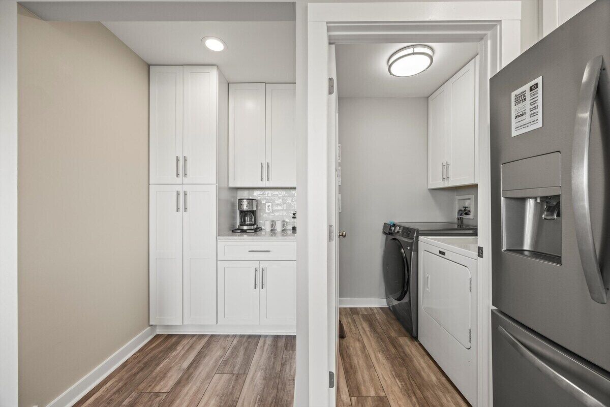 A compact kitchen with white cabinets, a stainless steel refrigerator, a coffee maker, and a washing machine.